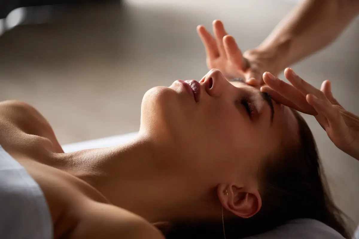 Woman relaxing on a treatment couch receiving a facial massage from a therapist's hands